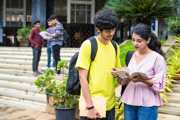 Serious indian teenager students preparing for exams by reading books at college campus - concept...