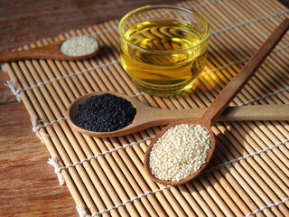 White and black sesame seeds in wooden spoon and a glass of oil
