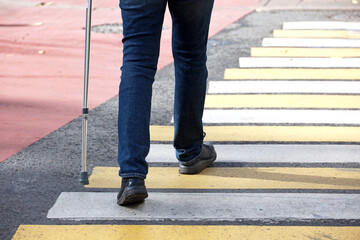 Man walking with a cane on crosswalk. Male legs in jeans on pedestrian crossing, street safety