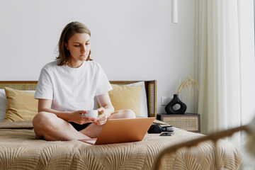 Obraz na płótnie Canvas young woman at home in casual clothes works remotely on a laptop while sitting on the bed. freelancer working from home