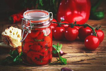 Baked canned red paprika pepper, marinated  with chili, garlic and herbs in glass jar. Rustic wood kitchen table background