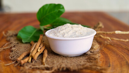 Roots and powder of Ashwagandha known as Withania somnifera in white bowl on wooden background. Indian ginseng, poison gooseberry, or winter cherry. Herbal adaptogen ayurvedic medicine.