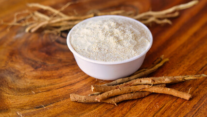 Roots and powder of Ashwagandha known as Withania somnifera in white bowl on wooden background. Indian ginseng, poison gooseberry, or winter cherry. Herbal adaptogen ayurvedic medicine.