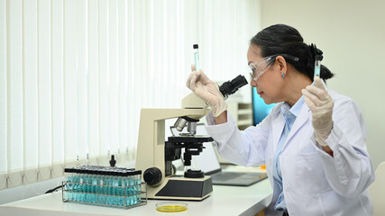 Professional senior female researcher looking under microscope, conducting experiment in a laboratory