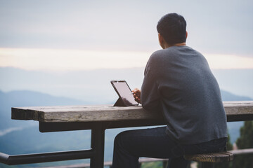 Freelancer guy using laptop tablet while is sitting against mountain scenery during vacation holiday in summer journey.Concept of travel and online working.