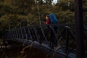  A caucasian man with a backpack walking on a bridge in the forest.