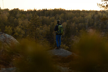 Fototapeta na wymiar A man with a backpack standing on a rock in the forest at sunset.