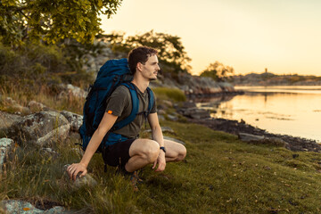 A caucasian man hiking by the sea with a backpack at sunset.