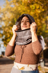 Outdoor fashion portrait of young Latin American woman with headscarf, posing in a park in autumn