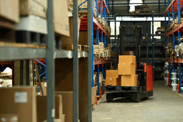 Forklift truck parking in large logistic distribution warehouse full of shelves with cardboard boxes