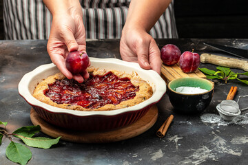 Homemade plum pie. A woman cuts a plum cake with a knife, Food recipe background. Close up