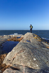 A caucasian man hiking on a rock by the sea with a backpack