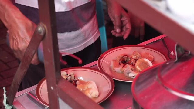 An Indonesian man street food vendor serves a customer in outdoor market. A man preparing a dish called 'Batagor' to customer on the street of Malang.