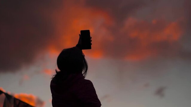 Silhouette of a Teenager Indian girl taking selfie with mobile phone during the sunset. Social media influencer creating content during sunset. Female posing for Selfie