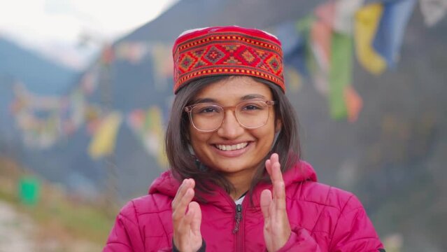 Portrait of happy smiling Indian woman wearing Himachali Cap standing in background of Himalayan mountains and doing Namaste. Positive emotion in a young Female. Indian tradition of greeting people.