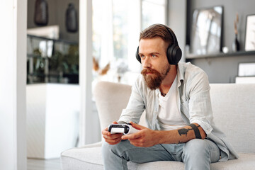 Young bearded man playing video games while sitting on the couch at home