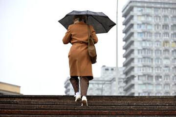 Woman with umbrella walking up the steps on buildings background. Rain in autumn city