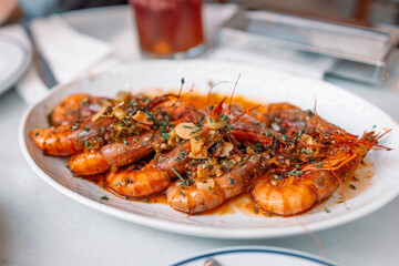 Traditional Spanish tapas. Aromatic delicious grilled king prawns with herbs and garlic pepper sauce on a white plate in a restaurant. Spanish cuisine dish.  - Powered by Adobe