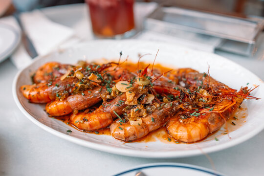 Traditional Spanish tapas. Aromatic delicious grilled king prawns with herbs and garlic pepper sauce on a white plate in a restaurant. Spanish cuisine dish. 