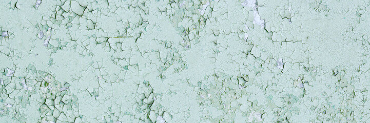 Peeling paint on the wall. Panorama of a concrete wall with old cracked flaking paint. Weathered rough painted surface with patterns of cracks and peeling. Wide panoramic grungy texture for background