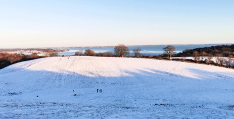 Danish winter landscape with white fields and hills close to the sea and children sledging in the snow