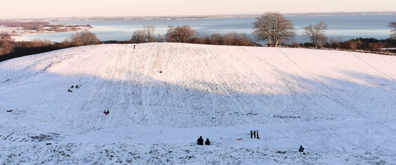 Danish winter landscape with white fields and hills close to the sea and children sledging in the snow