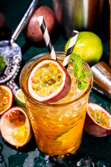 Sweet colorful tropical cocktail with passion fruit, lime and mint. Long boozy alcohol passion fruit drink over dark background copy space