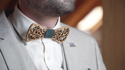 Groom in gray suit and with stubble adjusting wooden bow tie, close up.