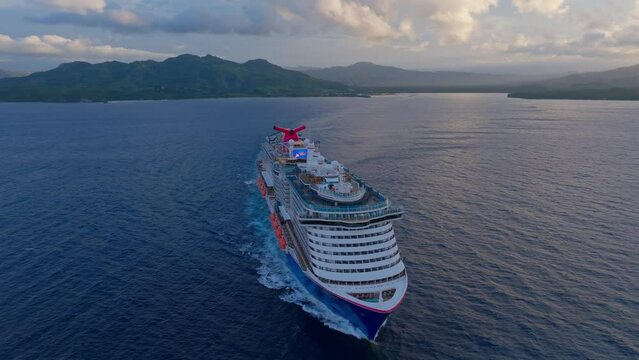 Aerial orbit shot of cruising cruise ship with luxury pools and tv monitor on rooftop in Dominican Republic - Sunset time and clouds at sky