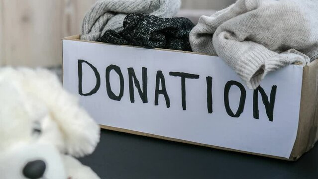 4k zoom in out Donation box with old used toys and clothes indoors. Happy Charity. Box with clothes in it. close-up. Clothing donation. Winter clothes in a cardboard box. Seasonal clothing