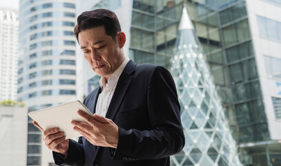 Low Angle View Of Serious Asian Businessman Using A Digital Tablet In The City