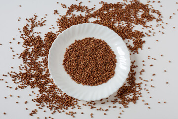 There are buckwheat grains on the table in a plate. On a white background.
