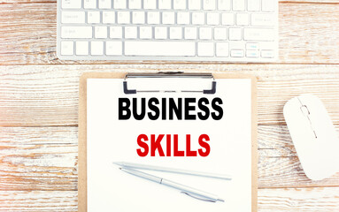 BUSINESS SKILLS text on a clipboard with keyboard on wooden background