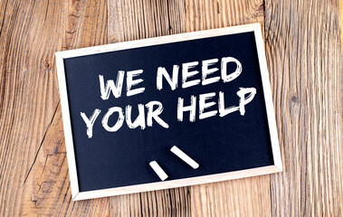 WE NEED YOUR HELP text on a chalkboard on the wooden background