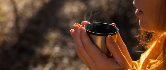 A woman holds a thermos of hot tea in her hands on a cold autumn day.