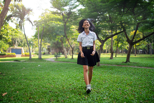 Portrait photo of a young asian beautiful female thai university student lady running happily and relaxingly in a park