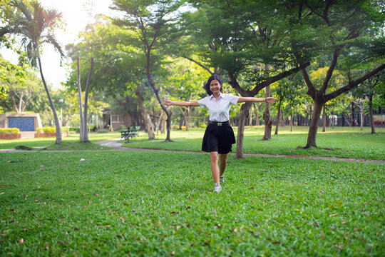 Portrait photo of a young asian beautiful female thai lady in her university student uniform running happily and relaxingly in a park