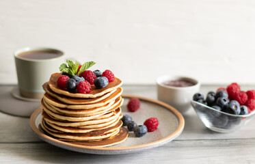 Pancakes with raspberries, blueberries, mint, jam and tea on light background
