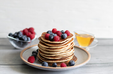 Pancakes with raspberries, blueberries and honey on a light background