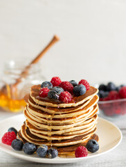 Pancakes with raspberries, blueberries and honey on a light background close-up