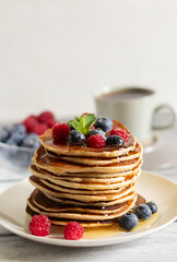 Pancakes with raspberries, blueberries and tea on a light background close-up