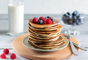 Pancakes with raspberries, blueberries, milk on wooden board with knife and fork