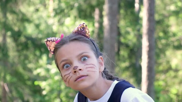 a girl with a make-up on her face, the image of a cat for halloween, preparation for the holiday of halloween, cat ears on a headband and a painted mustache and nose of a cat on a limpet