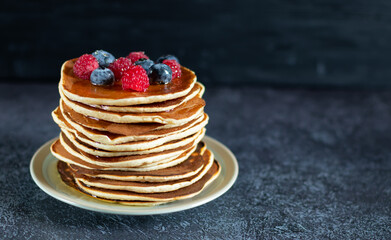Pancakes with berries and honey on dark background with copy space