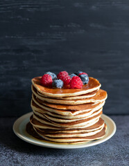 Pancakes with berrie and honey on dark background close-up, centered