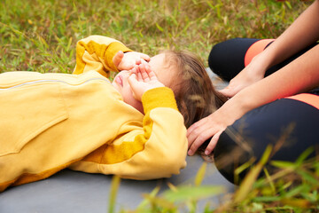 A smiling young girl in a yellow hoodie in the forest with yellow flowers in her hair. Rest on a meadow in the forest. Adorable child on a warm day on a mat