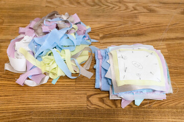 heap of cut-out pieces of silk fabrics with fixed paper patterns prepared for patchwork on wooden...