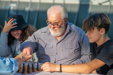 Grandparents and grandchildren playing board games outdoor on a sunny afternoon.