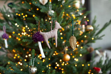 Close up of christmas tree with beautiful christmas lights and unusual decorations: golden balls, deer, fly agaric. Christmas background. Selective focus.
