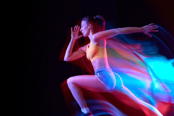 Speed. Professional female athlete, runner in motion over dark background in mixed neon light. Art,...
